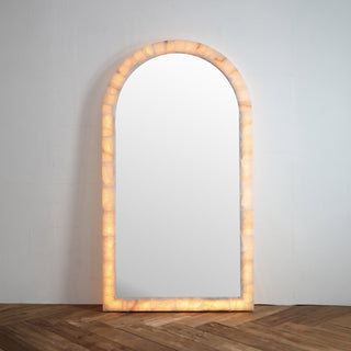 front view of Calista arched oversized floor mirror with natural stone frame and warm LED backlighting on wood floor