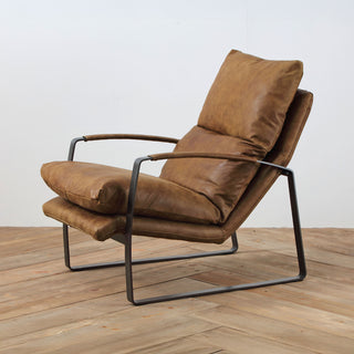angle view of whiskey leather lounge chair with steel base on wood floor