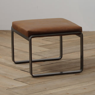 angle view of light brown leather lounge footstool with matte metal base on wood floor