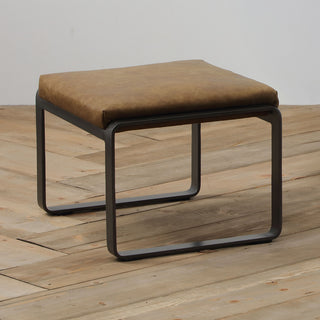 angle view of whiskey leather lounge footstool with matte metal base on wood floor