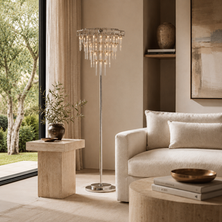 Aura floor lamp with tiered clear glass rods and a polished chrome finish beside a cream sofa in a modern living room.