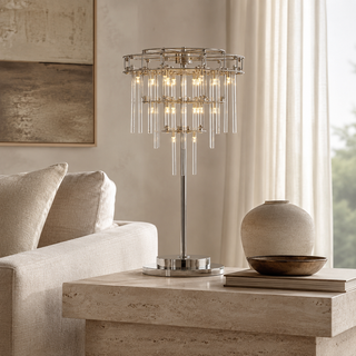 Aura table lamp with tiered clear glass rods and a polished chrome frame in a neutral luxury living room, illuminated with warm light, styled on a stone side table in a bright living room next to a sofa.