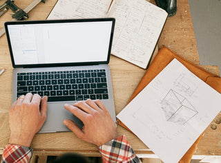 Interior designer working on laptop with floor plan sketches, notebook and coffee on wooden desk