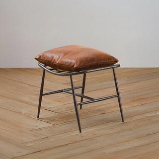 angled view of light brown leather footstool with vintage metal legs on wood floor