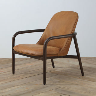 angle view of cognac leather armchair with minimal curved wood frame on wood floor