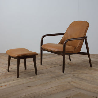 angle view of cognac leather armchair and ottoman with minimal curved wood frame on wood floor