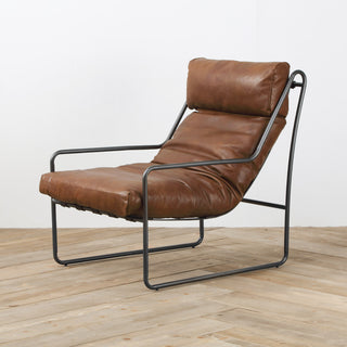 side angled view with wood floor background of modern light brown leather accent chair with metal frame