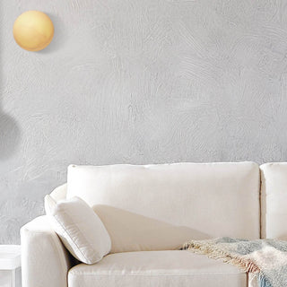 Moonlit Sconce softly glowing on a light-toned wall above a modern cream sofa in a minimalist living room setting