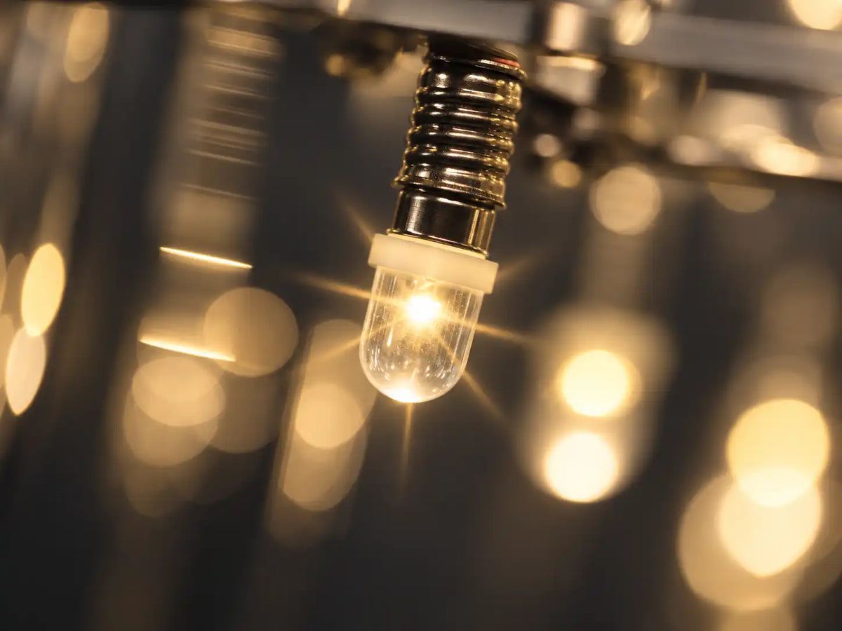 Close-up of an LED bulb on a modern ring chandelier, with a soft starburst and warm, blurred background lights.