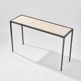 High three-quarter view of the calcite console table showing the tabletop depth, natural veining, and four slim black legs.