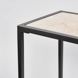 Corner detail of the console table showing the inset calcite top, black frame joint, and slim leg.