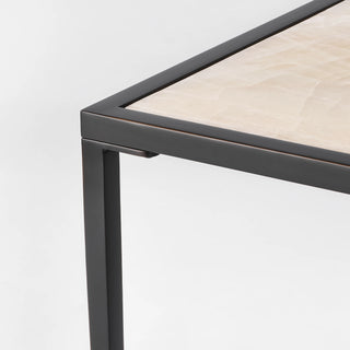 Close-up of the calcite side table corner showing the stone top, slim black frame, and leg connection.