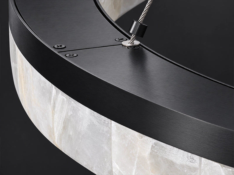 Macro of the Calista chandelier's black iron rim and suspension cable over pale calcite. Black and stone modern pendant light