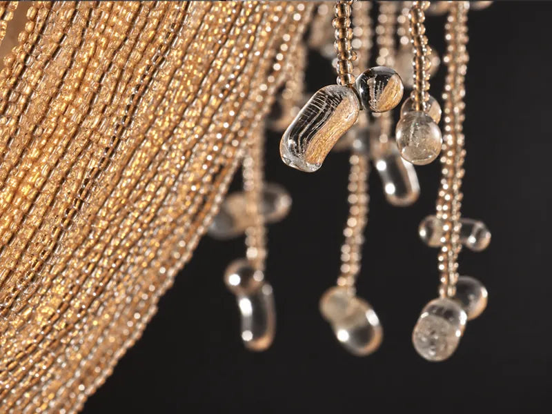 Close-up of the lit Cascade chandelier: warm light through strands of small glass beads and clear glass drops. Beaded glass chandelier