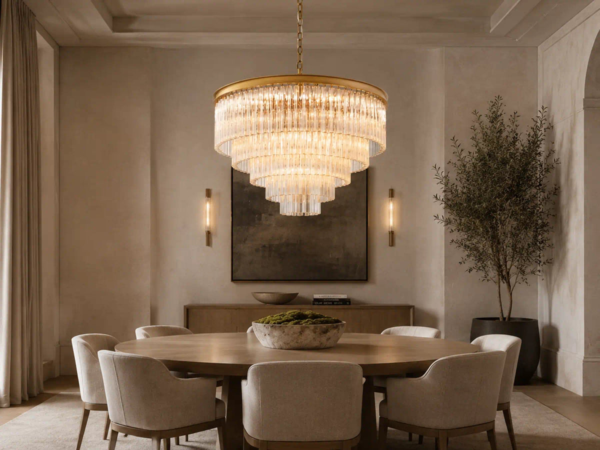 Marais Glass Chandelier casts warm light over a round wood dining table in a neutral-toned dining room with upholstered chairs and an arched window.