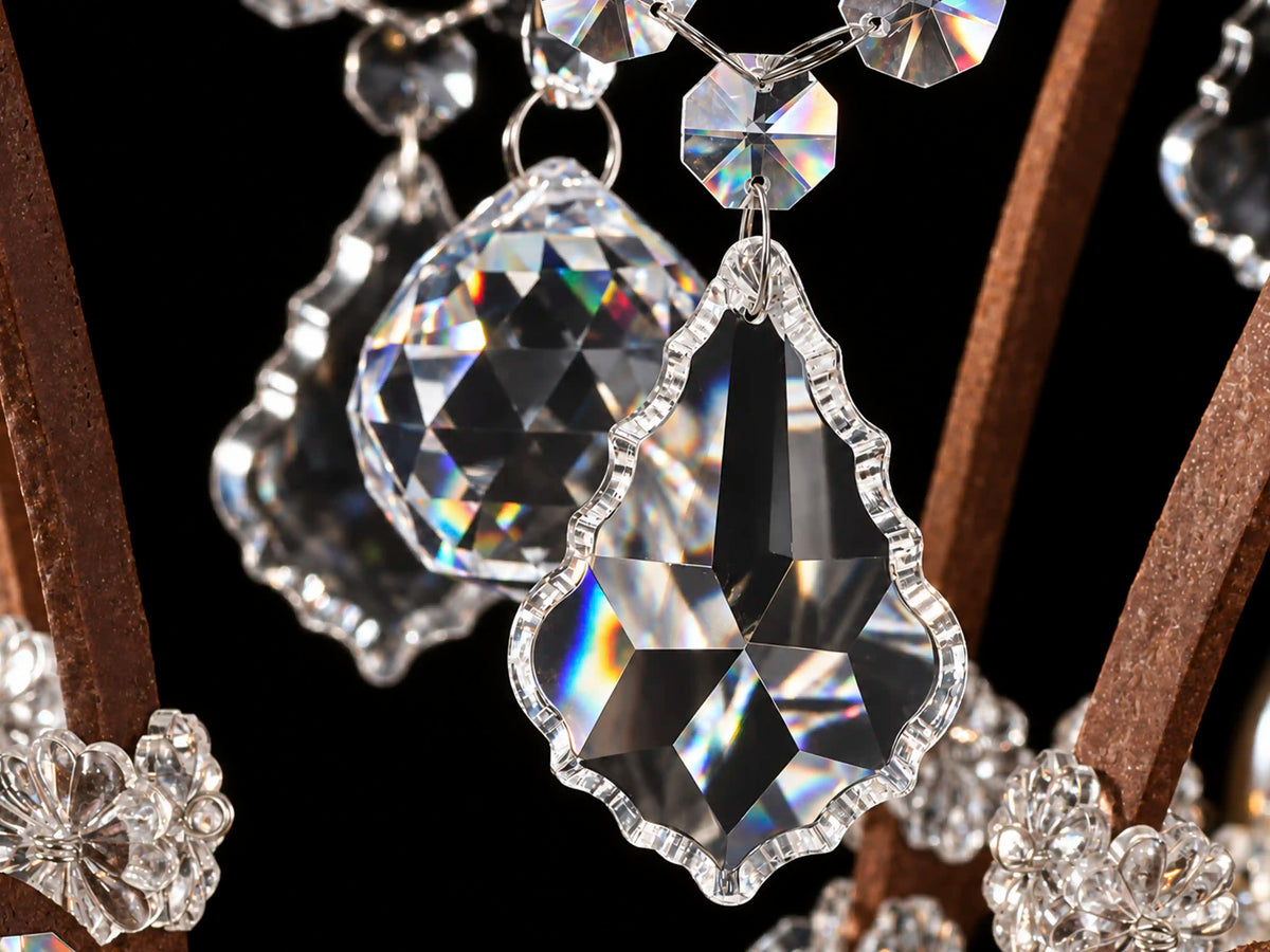 Close-up of faceted crystal pendants with soft warm reflections and rainbow highlights on a rust-finished iron chandelier against a black background.