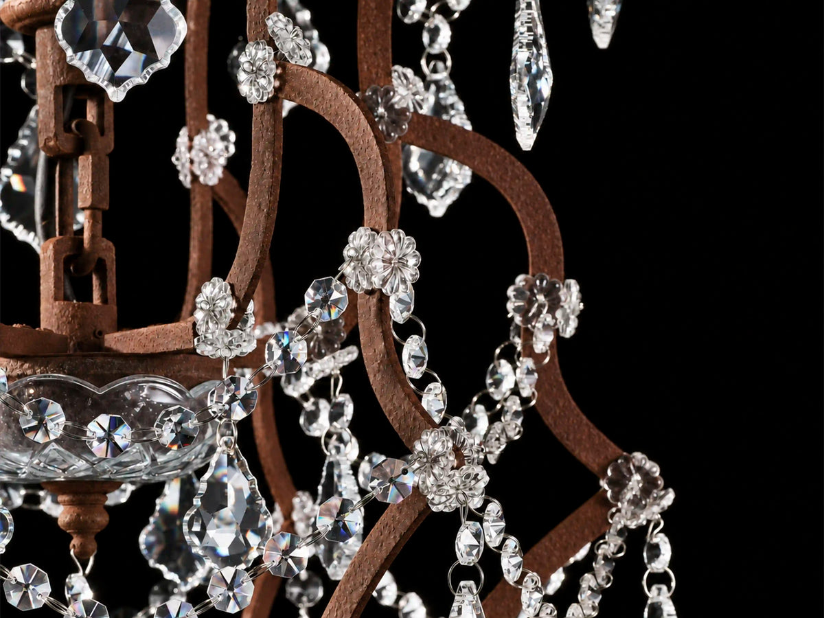 Close-up of the Rustline chandelier’s textured rust-finished iron frame, clear crystal rosettes, and faceted bead strands against a black background.