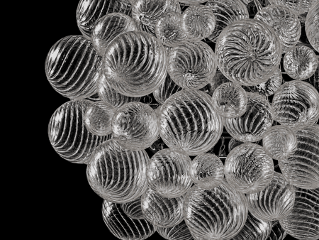 Close-up of the lit Spiral Bubble chandelier: mixed-size spiral-ribbed glass globes glowing warm against a black background