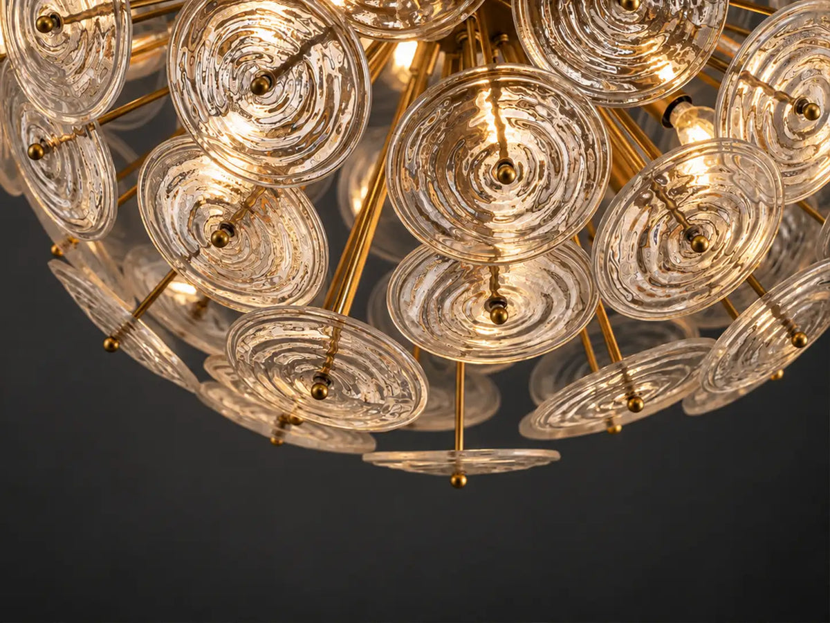 View from below of a globe chandelier with overlapping rippled glass discs, warm lights and a brass-finish frame against a dark gray background.