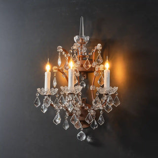 Warmly lit Moorizon Rustline 3-light wall sconce with candle-style bulbs, cascading crystal accents, and ornate iron frame on a dark background