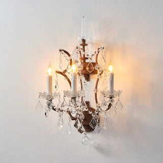 Warmly lit Moorizon Rustline 3-light wall sconce with candle-style bulbs, curved iron arms, and hanging crystal accents on a white background