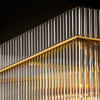 Lit Timelore Rectangular Chandelier close-up showing individual clear glass rods suspended from a warm brass rectangular frame in a black background.