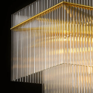 Lit angled detail of the Timelore Rectangular Chandelier with rows of individual glass rods and a warm brass frame in a black background. 