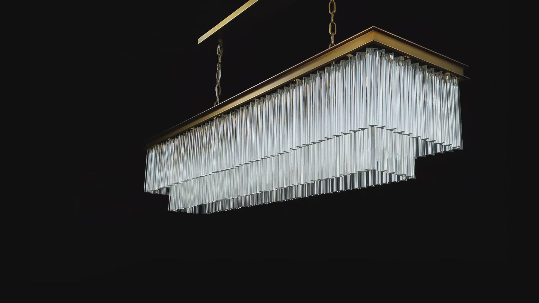 Marais Rectangular Glass Chandelier shown from multiple angles, with warm light passing through tiered clear glass rods and a brass-finished frame.