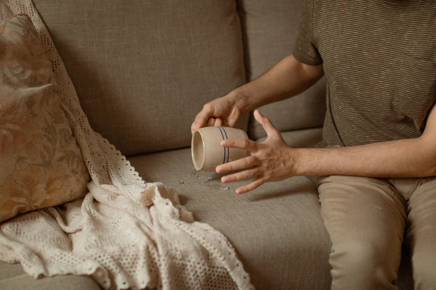 Person accidentally spilling a drink on a beige fabric sofa, close up of living room upholstery spill